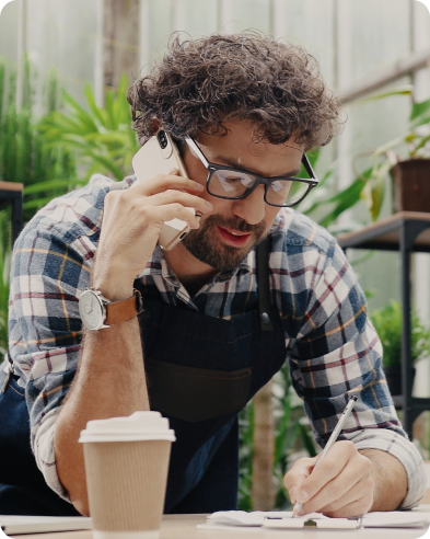 desktop-claims A man in a plant nursery talks on the phone while writing notes.