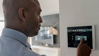 A man in a blue shirt ensures the doors in his house are locked using a home security system.
