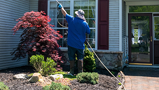 A man with a water hose power washing the roof and siding of a house