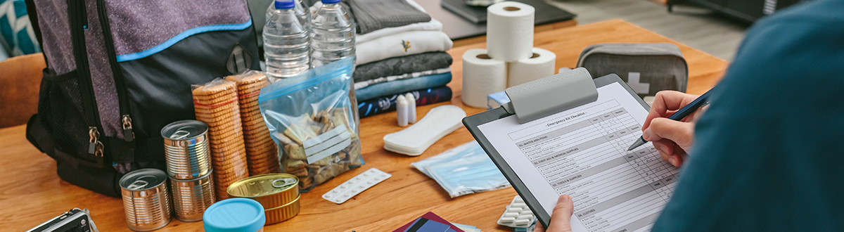 Close up of home emergency supplies near a person marking items off an emergency planning checklist